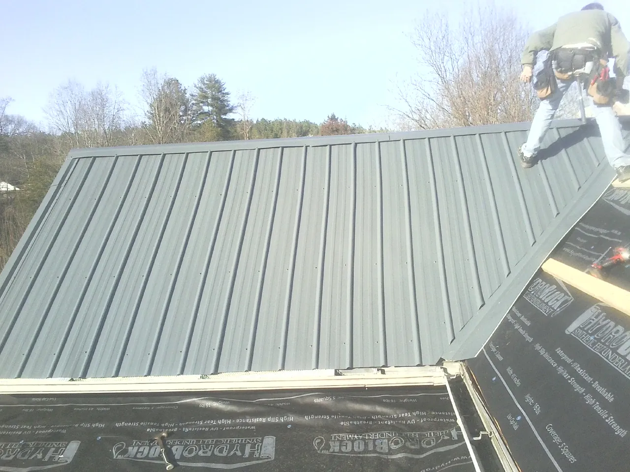 Crew installing dark green standing seam panels over synthetic underlayment in Hammond