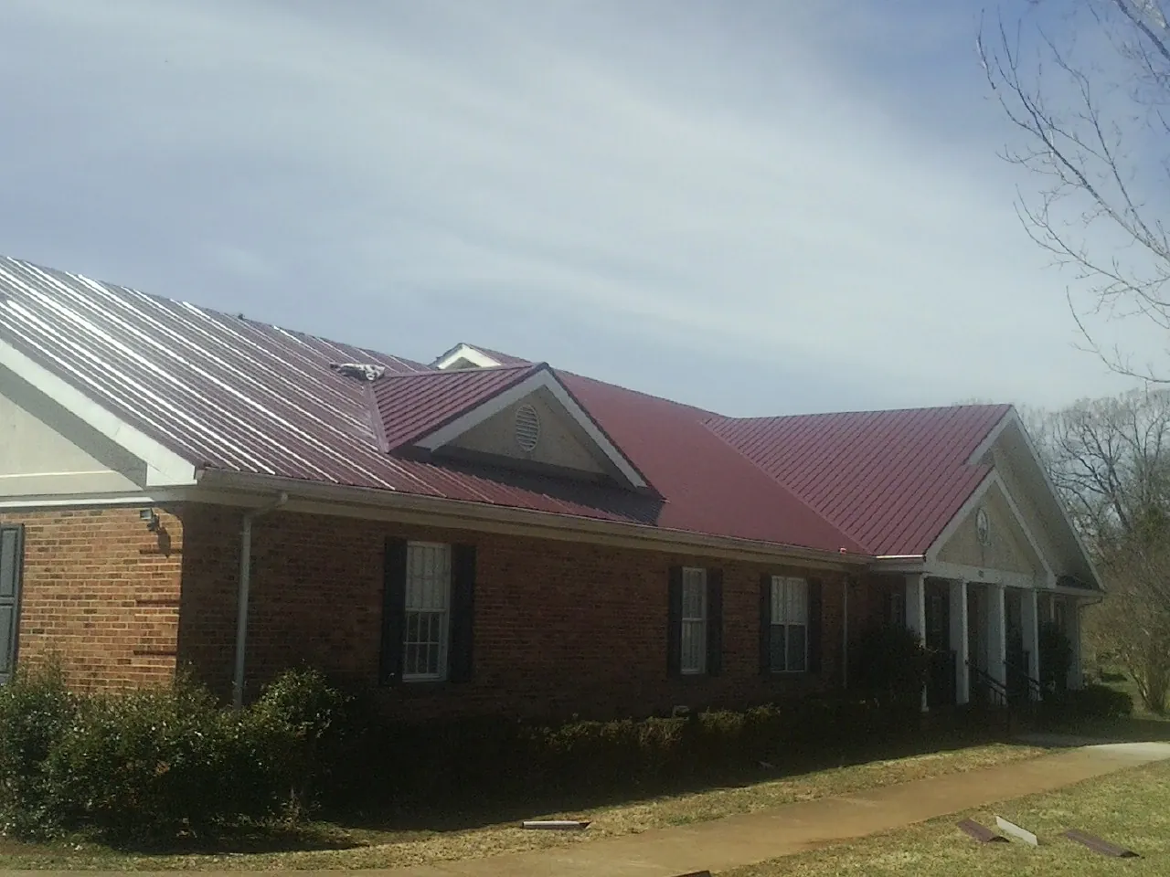 Red metal roof with gabled entries on a long brick building, from a Hail Damage Roof Repair job in Hammond